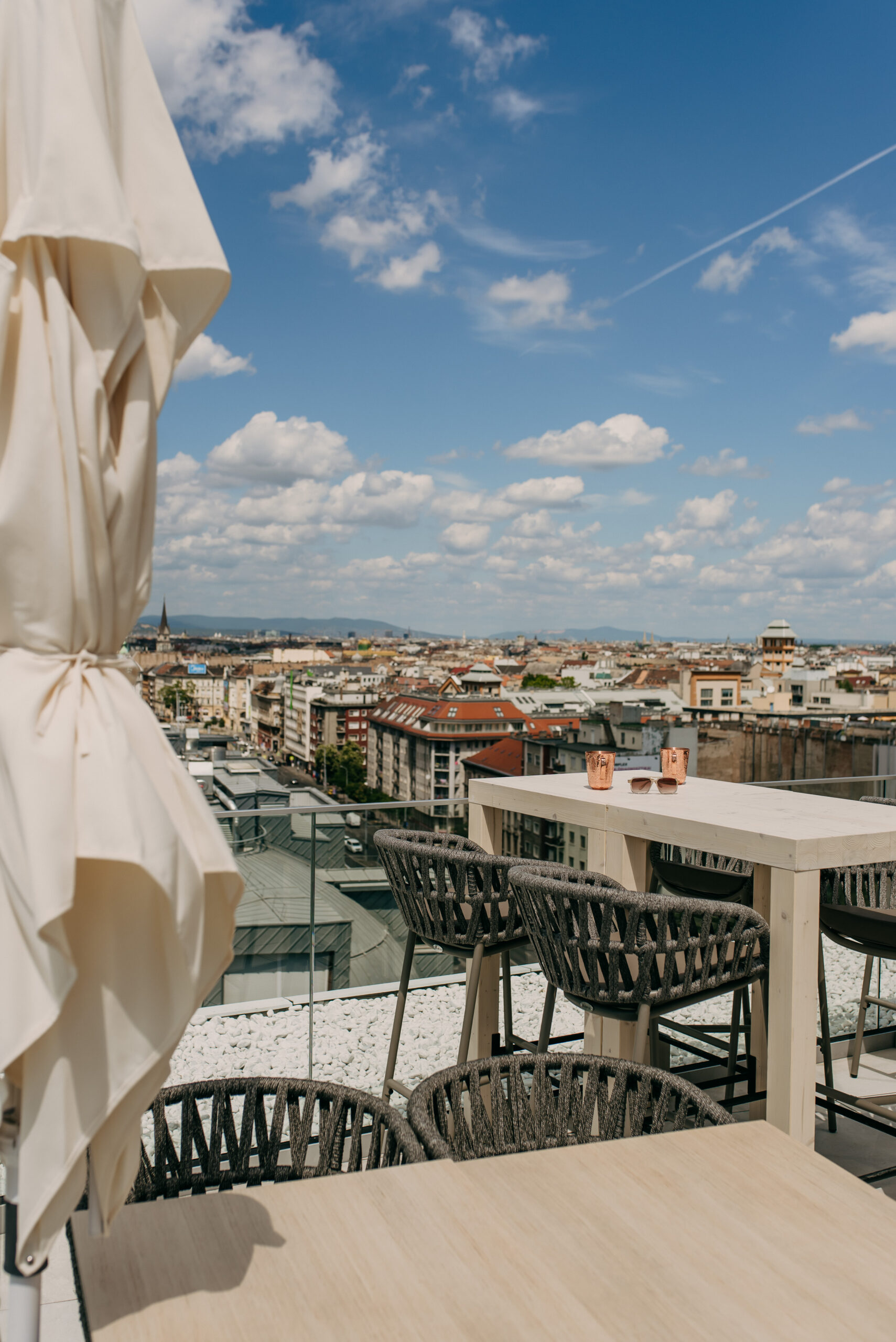 Panorámás kilátás Budapestre egy magasított asztallal és elegáns kültéri székekkel a Selva Skybar teraszán