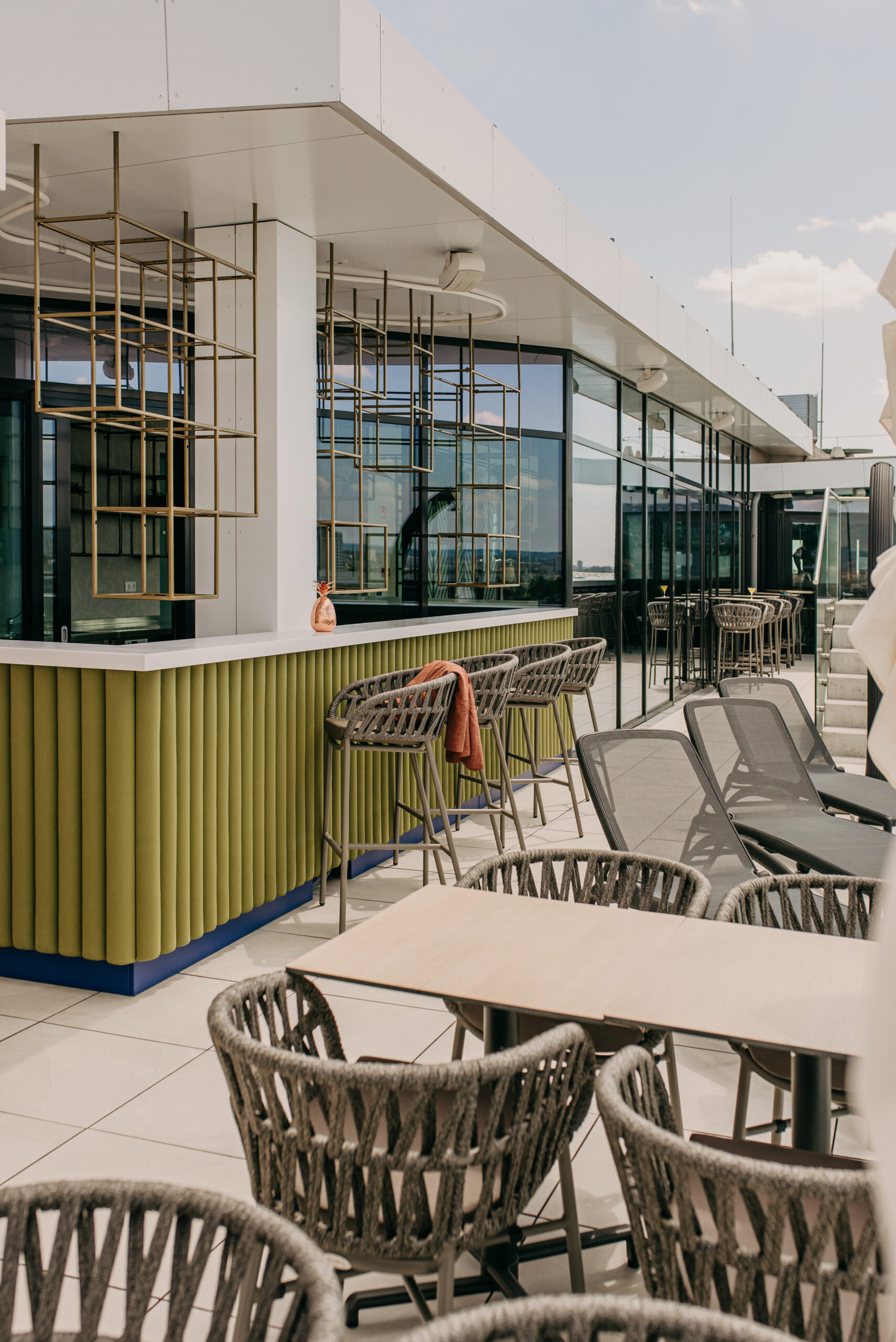Modern rooftop bár zöld pulttal, magasított székekkel és napozóágyakkal a Selva Skybar teraszán